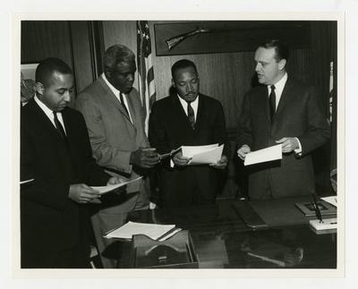 From left to right, Frank Stanley, Jr., Jackie Robinson, Dr. Martin Luther King, Jr., and Kentucky Governor Edward T. Breathitt reading legislative bill to desegregate public accommodations in Kentucky
