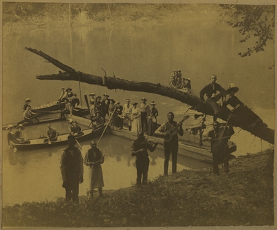 Men and women in boats at the waterside at Boone's Fort with a group of African American male musicians on the shore