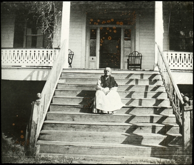 Unidentified African American woman sitting on the front steps of a large house