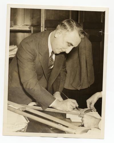 Vinson autographs the crutches of Frank N. Belgrano, Jr