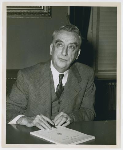 Secretary Vinson at desk with pen and congressional document