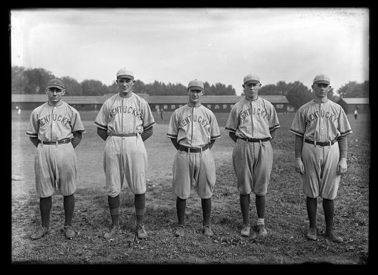 Five baseball players with long, low building in background