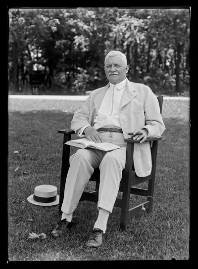 Professor M.A. Cassidy with book, cigar, in chair outside