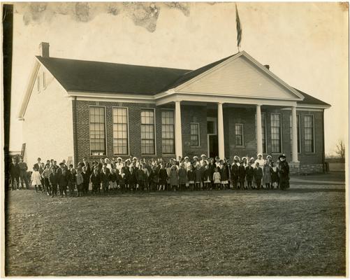 Group portrait of Athens students and Nannie Faulconer (1865?-1940) standing in front of the school. Handwritten on verso Type of School Building used in Fayette County Rural Schools. The Colonial suits the landscape of this particular County, Athens-Dist. No.18. Fayette County, Kentucky