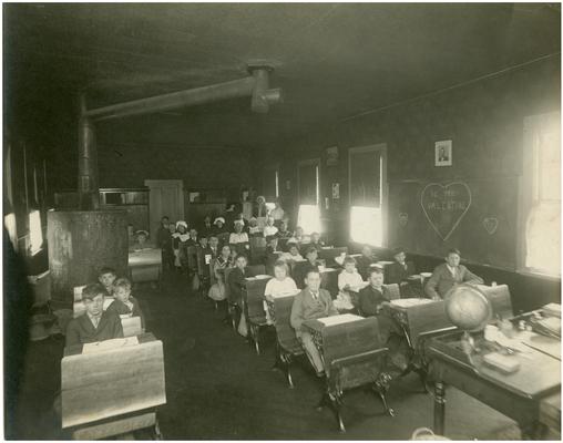 Cave Spring students sitting at their desks with Nannie Faulconer (1865?-1940) and teacher Rose Wurtele in the background. Handwriting on verso. (Four copies)