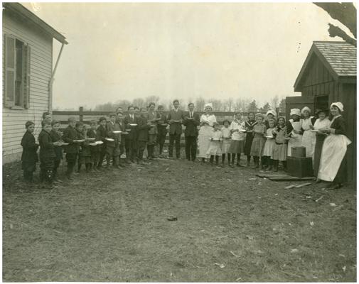 Cave Spring students being served lunch outside of the school house with Rose Wurtele and Nannie Faulconer (1865?-1940) (Two copies)