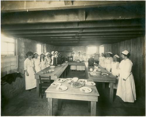 Group portrait of Athens' girls in cooking class with Nannie Faulconer (1865?-1940). Handwritten on verso on 3a The cooking class and an exhibit of their work at Athens, a rural school which twelve miles from Lexington, Fayette County, Kentucky. (Two copies)