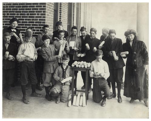 Group portrait of Picadome boys along with Nannie Faulconer (1865?-1940) and Margaret McCubbing examining ears of corn. Hand written on verso, Home and rural activities receive attention in Fayette County, Ky. In 1910. (Two copies)