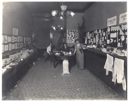 Portrait of Nannie Faulconer (1865?-1940) and Mrs. Marguerite McLaughlin at the school fair with displays of students' work. Handwriting on verso. (Three copies)