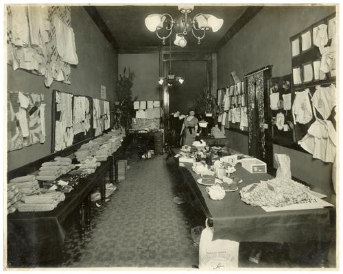 Portrait of Nannie Faulconer (1865?-1940) at the school fair with displays of the students' work (B). Handwritten on verso, Division A exhibit at the Rural School Fair given in Lexington Fayette County, Kentucky in 1912. (Two copies)