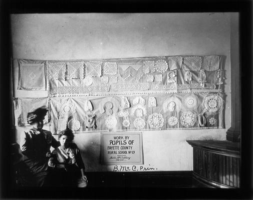 Handwork display by Picadome students. Sign reads Work by students of Fayette County rural school No. 19. Belle McCubbing, teacher