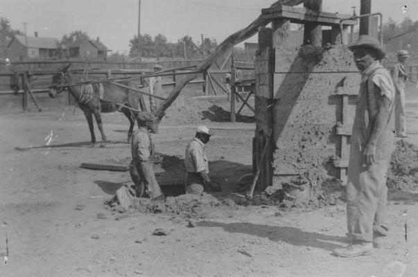 Project #1-73-27-68 District 1, Branch District 3: Photograph 2 in a series showing the various steps in manufacturing brick to be used in building a 10' wall around Keiler Athletic Field in Paducah, KY. Mixing clay by means of old fashioned mud-wheel. Materials are thoroughly mixed in box. Note power supplied by mule walking in circle