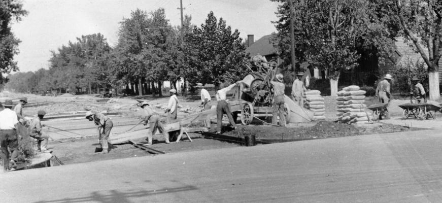 Projects #2372 and Project #2373 District 1: Projects #2372 and #2373 provide for the construction of a two-drive concrete pavement, with a park in the center, on Elm Street in Henderson, KY. Workmen pouring concrete during construction of a two-drive street with a park in the center. View photographed September 18, 1936