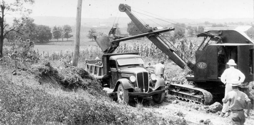 Master Project #2941 District 2: Under Master Project #2941 the reconstruction and repair of various roads in Boyle County are provided. View shows reconstruction of a rural road showing a small power shovel loading earth, photographed July 28, 1936