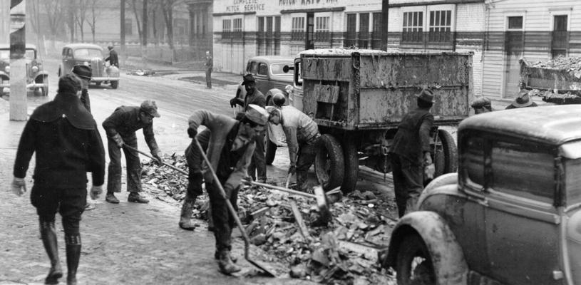 1937 Flood. Clean-up work in Louisville, KY. WPA workers cleaning up debris from 22nd Street, just north of Broadway. Note the water line on the buildings across the street. View photographed February 8, 1937