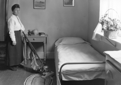 Interior of bedroom, woman with vacuum