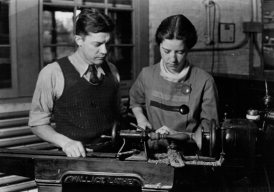 Woman using a lathe as instructor watches