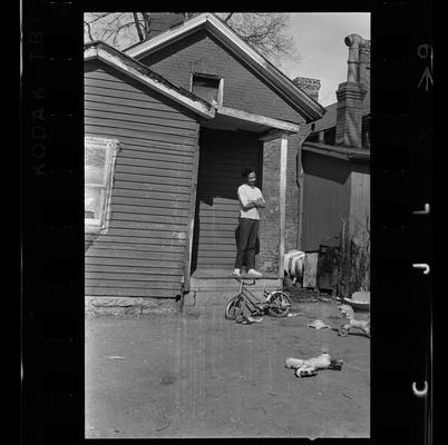 Four men behind fence, Woman on porch, Junk pile