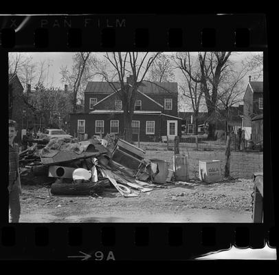 Four men behind fence, Woman on porch, Junk pile