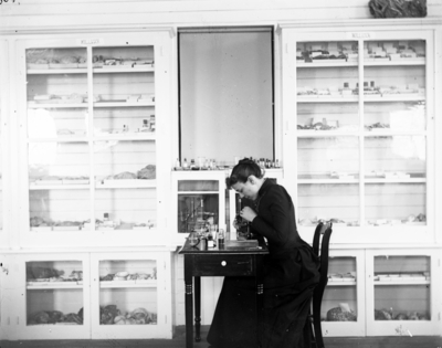 a woman sitting at a small table using a microscope