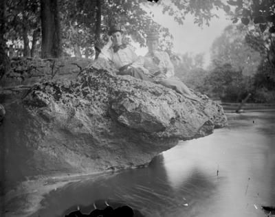 2 women sitting on rock that is jutting out over a body of water