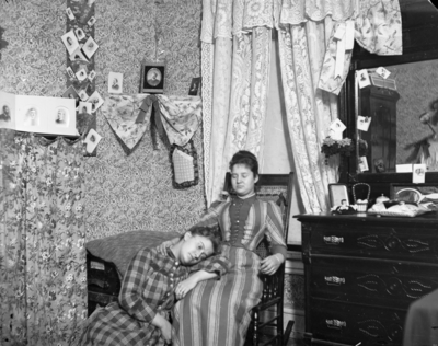 2 women, one woman is sitting in a rocking chair and the other woman is resting her head on the other woman's lap