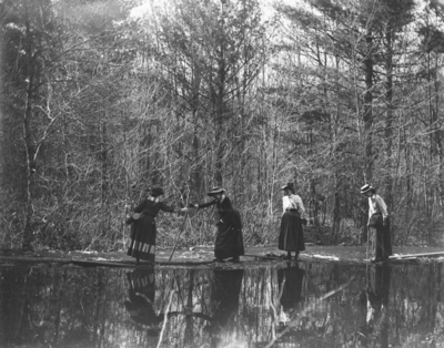 4 women helping each other cross what appears to be a small section of river