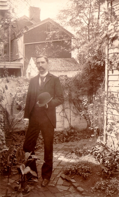 Charles Nourse Lyle standing in garden holding his hat