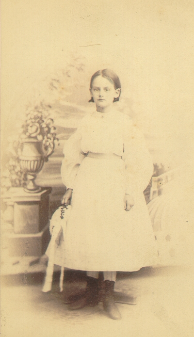 Helen Lyle wearing white dress in front of artificial scenic background