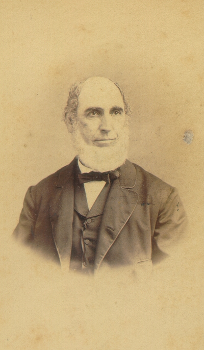 Elderly man with full white beard wearing dark suit with bow tie