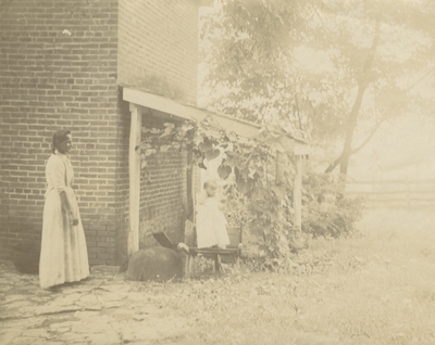 an unidentified woman and child, the child is standing in a wheel barrel