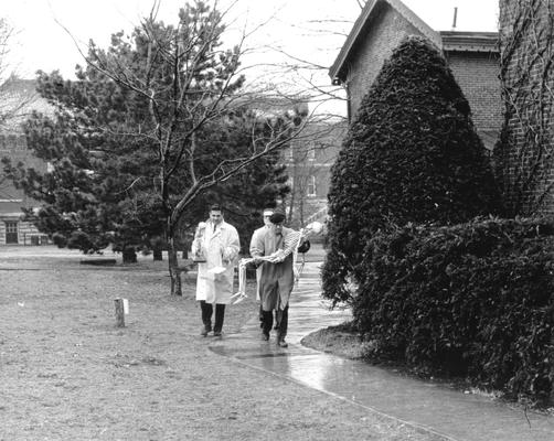 Dr. Snow, professor of anthropology, carrying a full human skeleton; two other men are unidentified