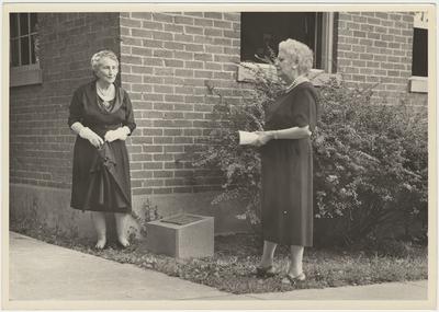 On the right is Former Students Association historian, Mrs. Pearl Day Bach. Her and another lady are dedicating a marker on the site where two Sarah K. Yancey Homes (dormitories for female students and staff) burned. The current (August 13, 1961) school and administration building they are standing by (library windows) was built by staff and students of bricks made and burned on campus Two women standing near a marker at the corner of a brick building (August 13, 1961)