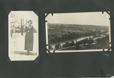 woman standing on the sidewalk, snow on the ground; view of a river and fields