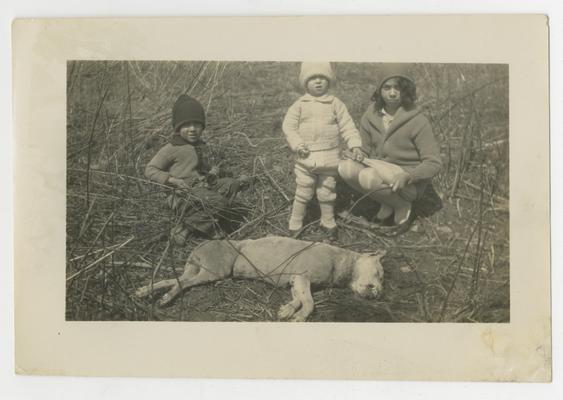 Three unidentified children crouching beside a dead dog