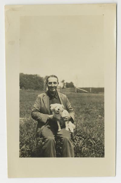 Unidentified man sitting on a chair in a field with a dog on his lap