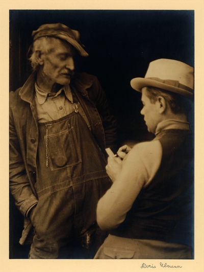 John Jacob Niles.  Elderly man in hat, coat, and overalls, and younger man (JJN) in hat and vest, taking notes