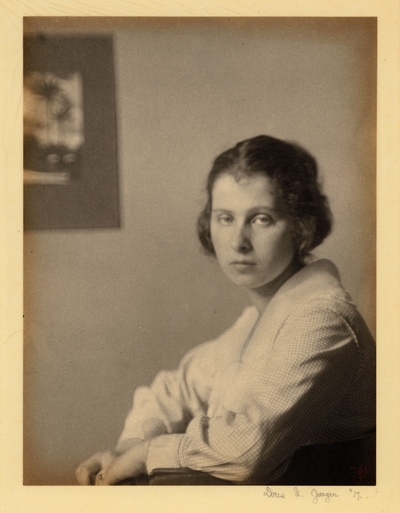 Young woman with head turned to look at camera, seated in chair, with picture hanging in background