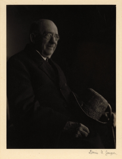 Elderly man in glasses and coat, seated with hat and cane