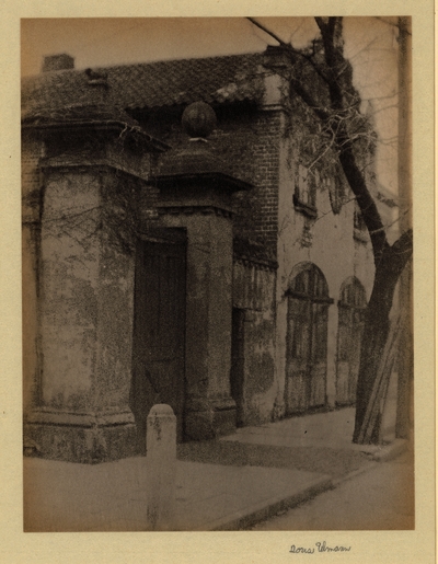 Brick and stone building with two arched wooden doors, tiled roof, and gate