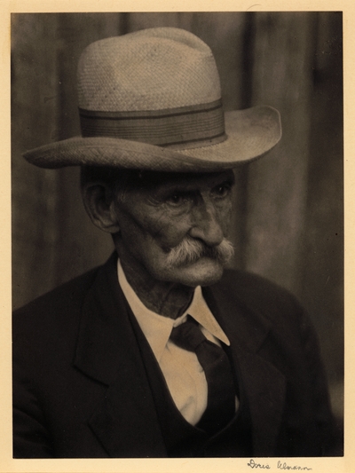 Head shot of elderly man with mustache, in hat, suit, and tie