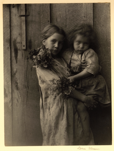 Young girl holding a younger girl who is holding two bouquets of flowers