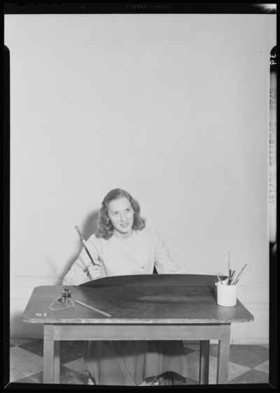 Georgetown College; Drucilla Corley sitting at desk holding                             paintbrush