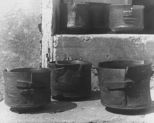 Six ceramic slab pots by John Tuska. Round shaped pots formed by slabs of clay bound together by another slab of clay. The pots are sitting on concrete steps. A different view of the pots in image 21