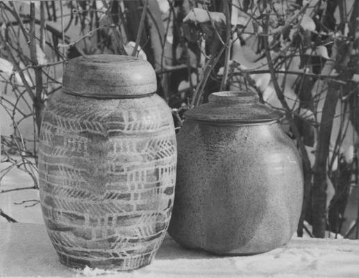 Two ceramic pots with a lids sitting in snow, pieces of John Tuska's Alfred University graduate work