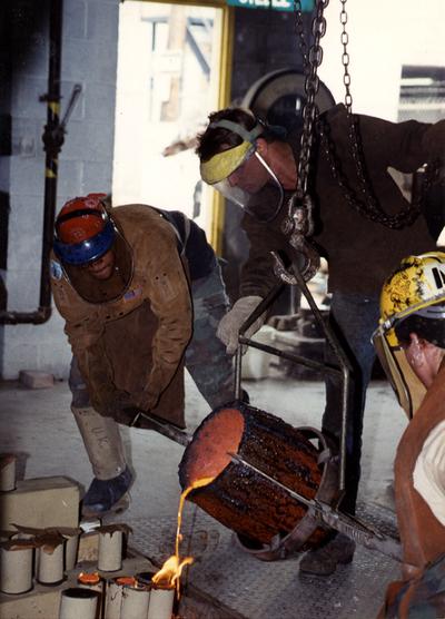 Scott Oberlink, an unidentified man and Andrew Marsh pouring bronze from a crucible in the University of Kentucky foundry for the casting 