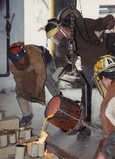 Scott Oberlink, an unidentified man and Andrew Marsh pouring bronze from a crucible in the University of Kentucky foundry for the casting 