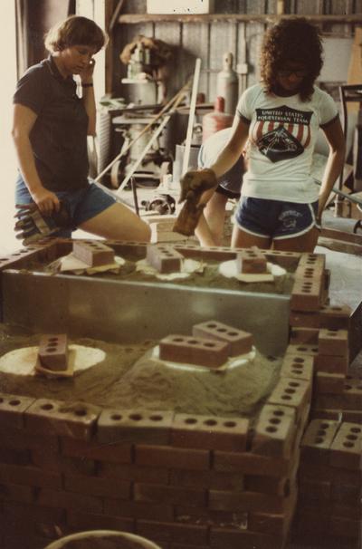 Three students preparing molds for a foundry class at the University of Kentucky. The photograph was taken by Ted Bronda