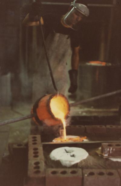 An unidentified person assisting with a pour for a cast at the University of Kentucky foundry. The photograph was taken by Ted Bronda