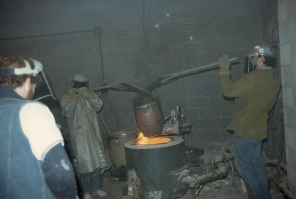 An unidentified man, John Tuska and Jack Gron putting a crucible in the furnace of the University of Kentucky foundry. The photograph was taken by Zig Gierlach